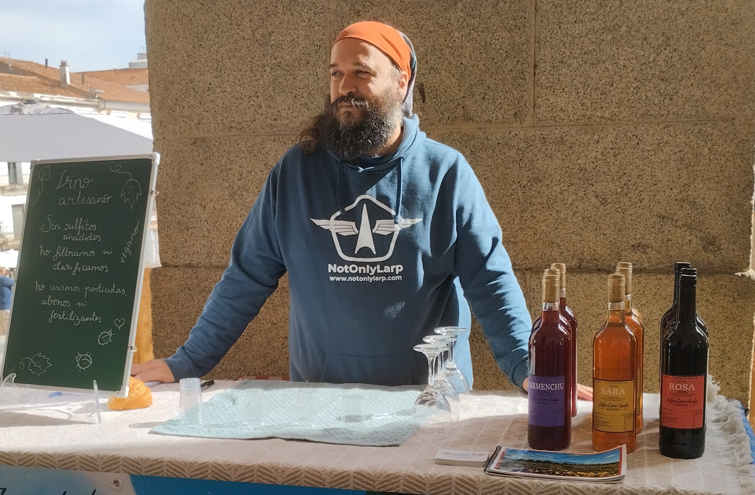 Un hombre con barba vende vino natural en un puesto de mercado.