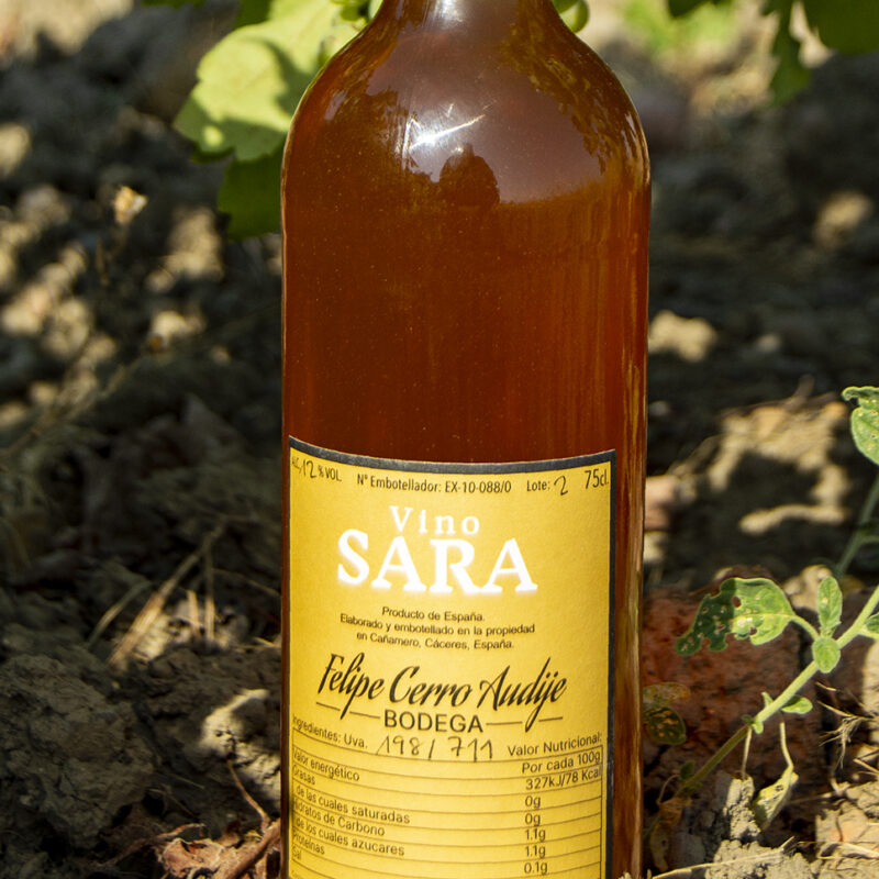 Botella de vino naranja con etiqueta amarilla donde pone Sara fotografiada junto a una viña.