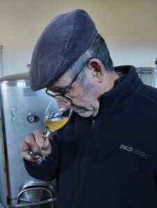 Un hombre con forro polar y boina cata un vino de color amarillo dorado